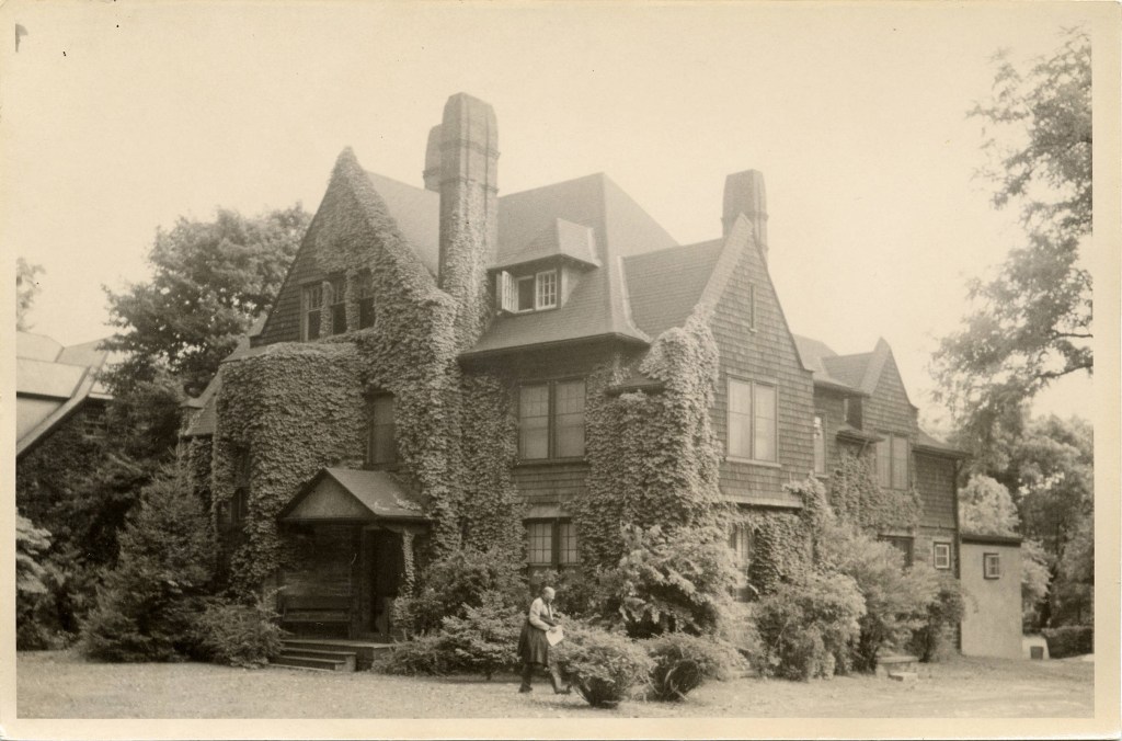 La imagen es una foto de la casa, tomada en 1902. Frente a la casa va pasando un hombre en mangas de camisa, llevando al brazo su chaqueta y con unos papeles en la mano.